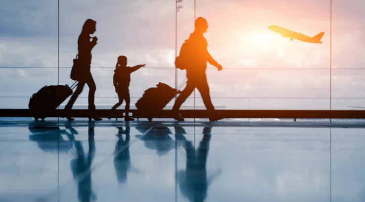 Silhouette of family walking through airport with plane taking off in background