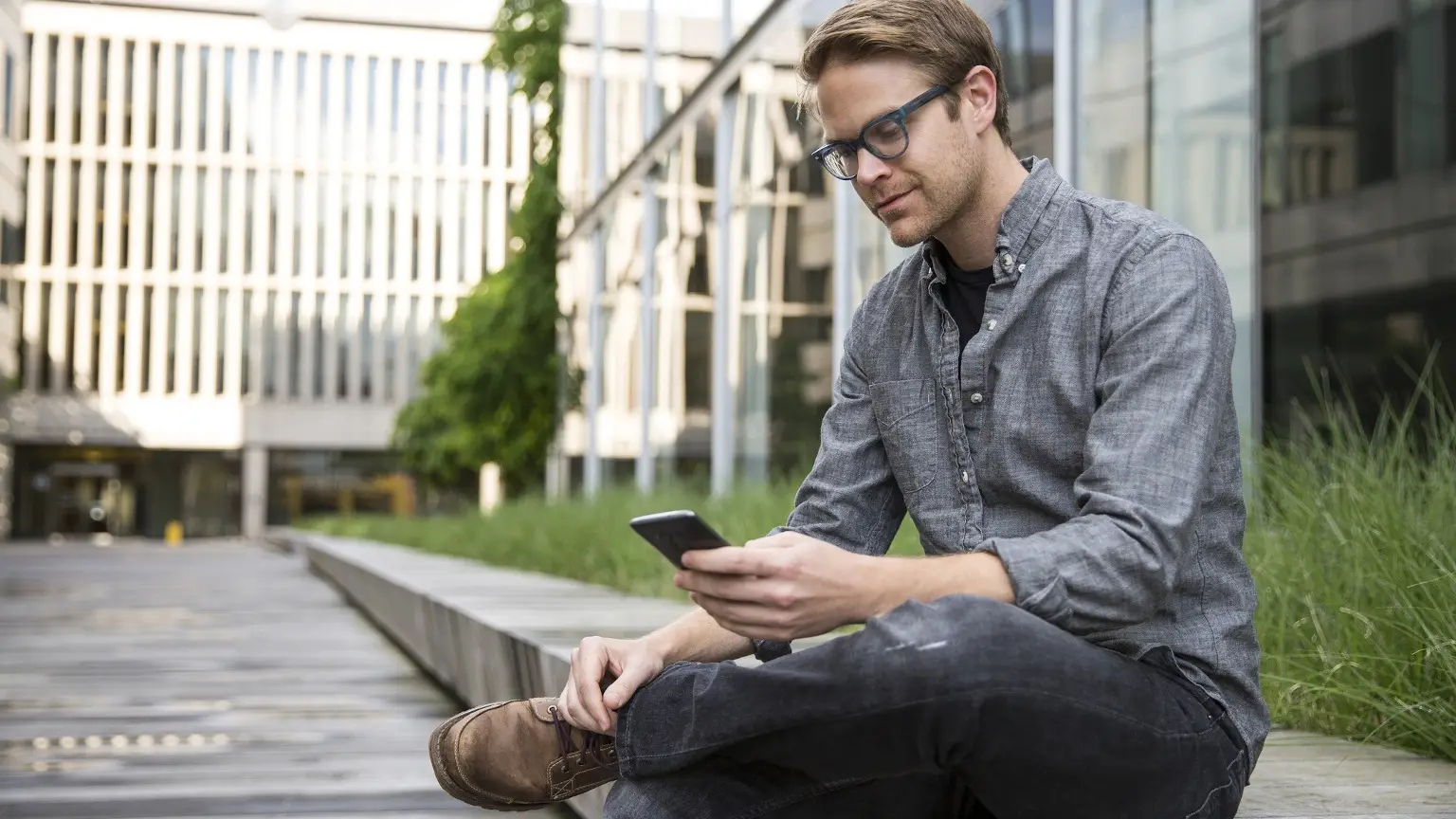 Image: Getty Images Man looking down on phone whilst sitting at a public park