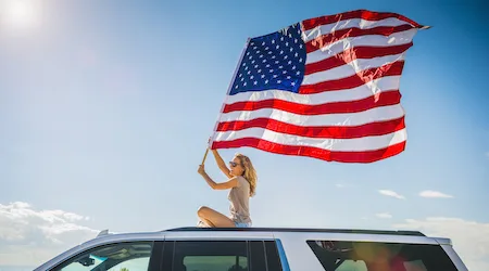 Hispanic woman waving American flag sitting on roof of white SUV Hispanic woman waving American flag sitting on roof of white SUV