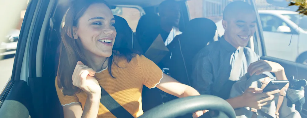 Happy young woman dancing with friends seen through car windshield on sunny day