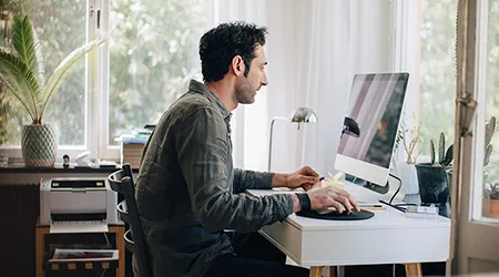 Side view of young businessman using computer while sitting at desk in home office Side view of young businessman using computer while sitting at desk in home office