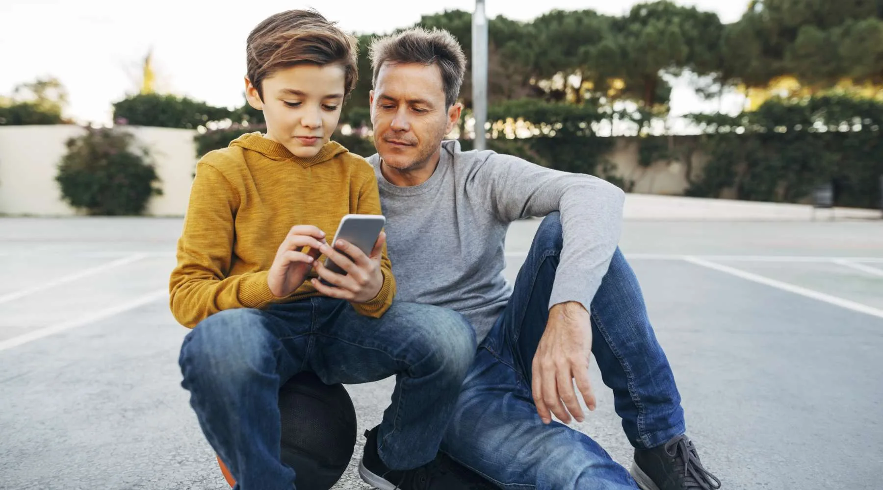 Father and son sitting on basketball outdoor court using cell phone Father and son sitting on basketball outdoor court using cell phone