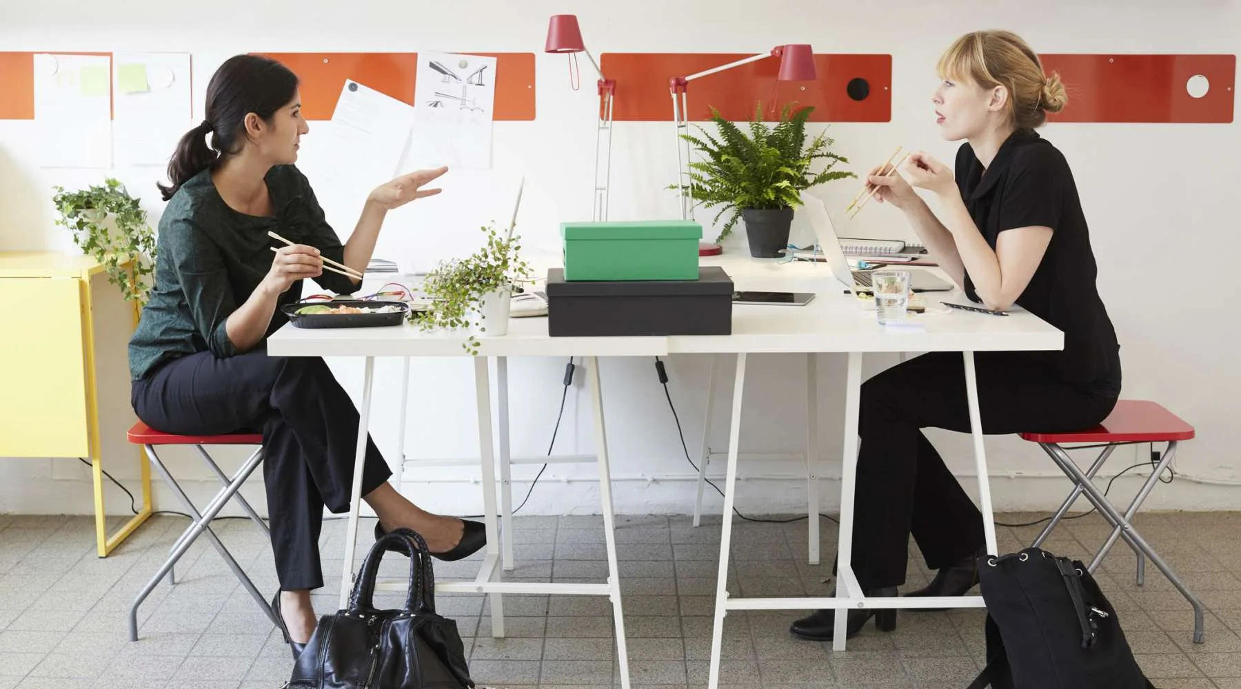 Full length of businesswomen talking while having lunch at table in office Full length of businesswomen talking while having lunch at table in office