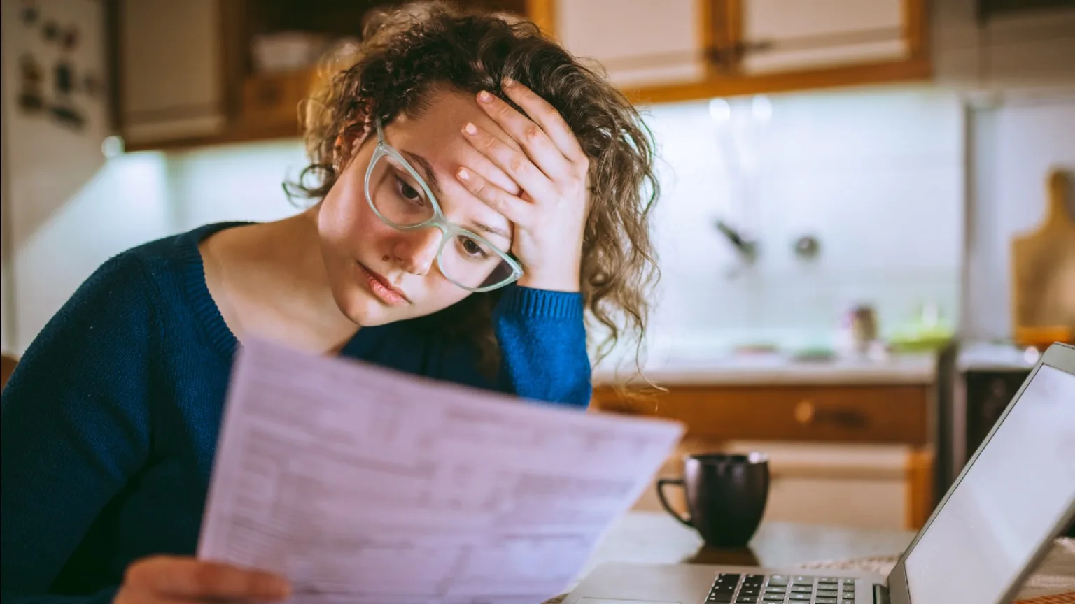 Image: Getty Images Worried woman with a computer looking over bills