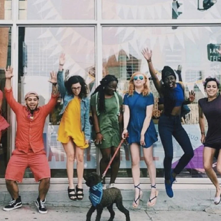Five women, one men and a dog jumping on the outside of a store
