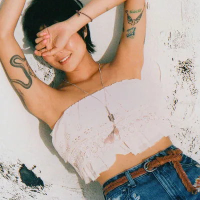 Tattooed asian woman liyng on the floor wearing a white top and blue jeans