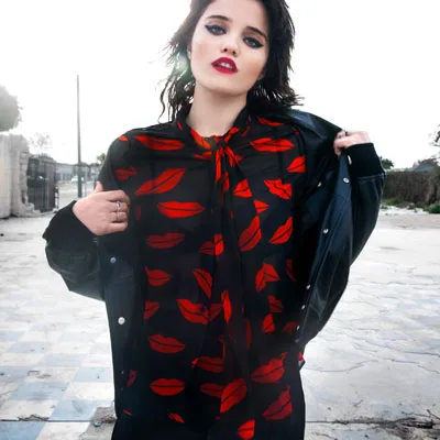 White female model with brown hair wearing a black shirt with printed kisses all over it