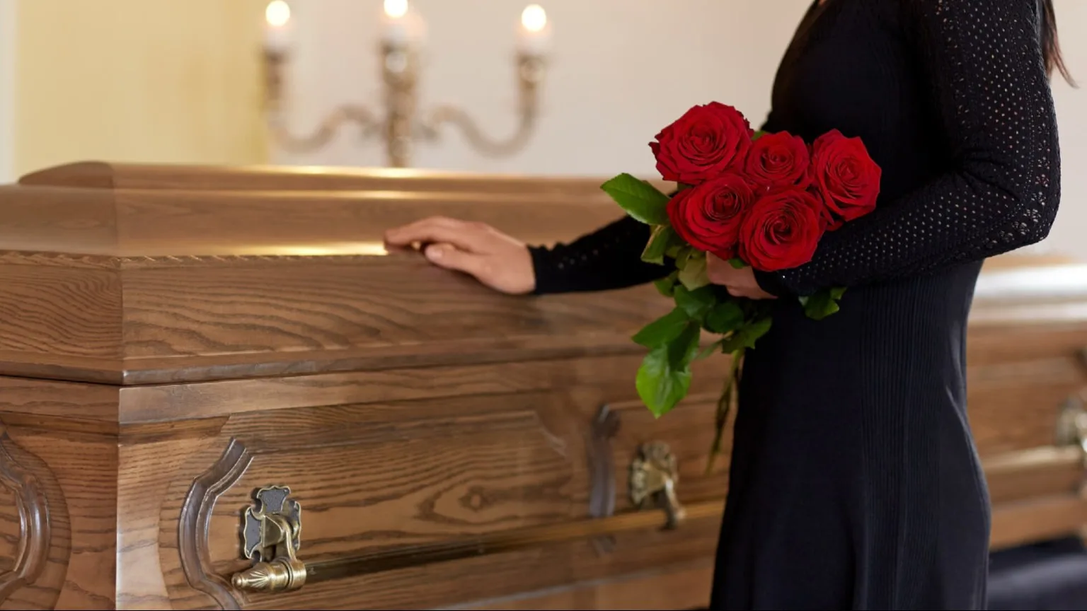 Image: Shutterstock Woman dressed in black with roses touching a coffin