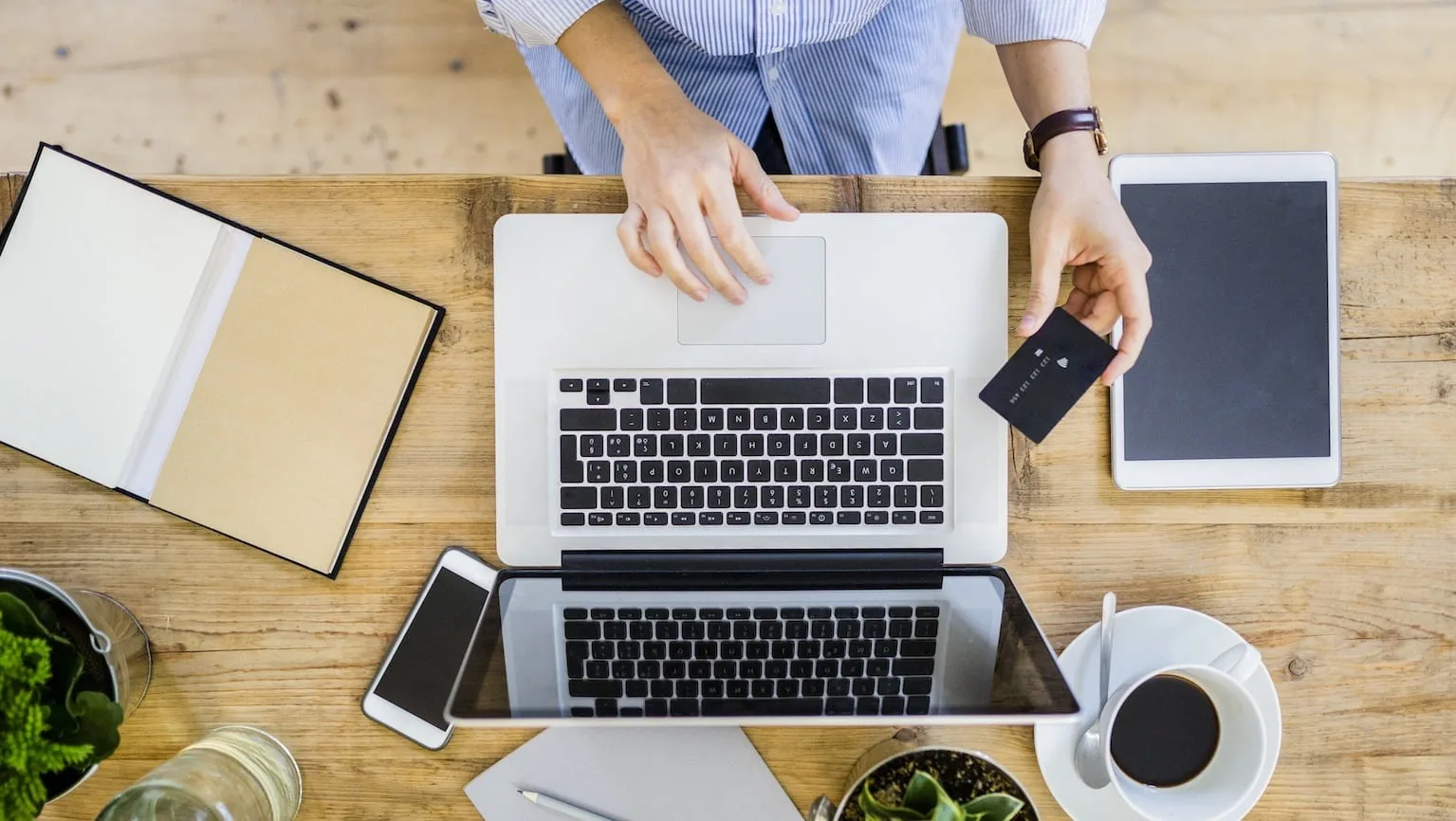 Image: Getty Images Top view of woman at wooden desk with credit card and laptop