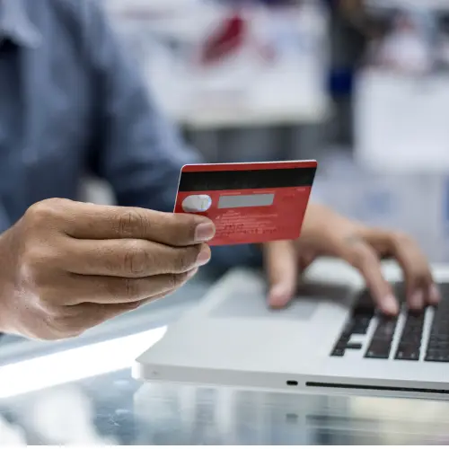 Man holding card while typing on laptop