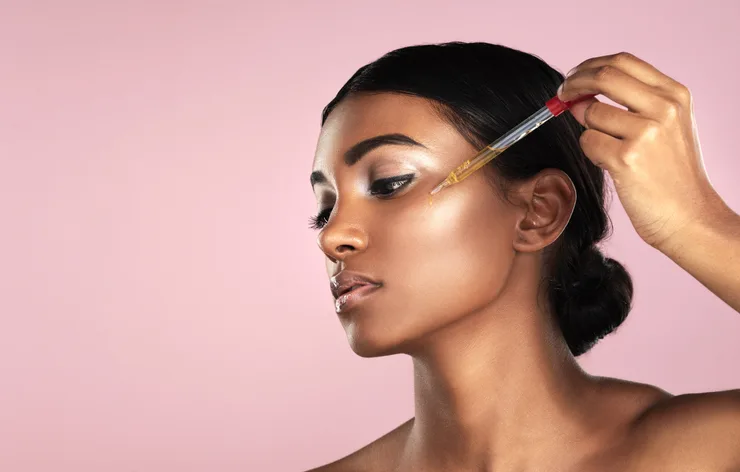 Image: Getty Images Studio shot of a young woman applying essential oil to her face with a dropper posing against a pink background