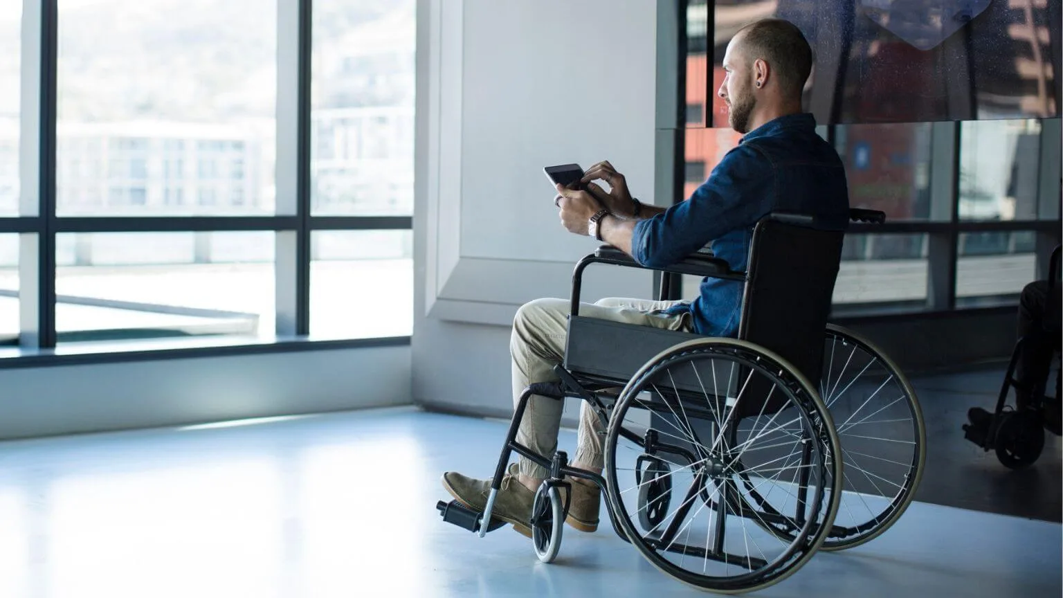 Image: Getty Images Man in wheelchair looking out of window in office using tablet