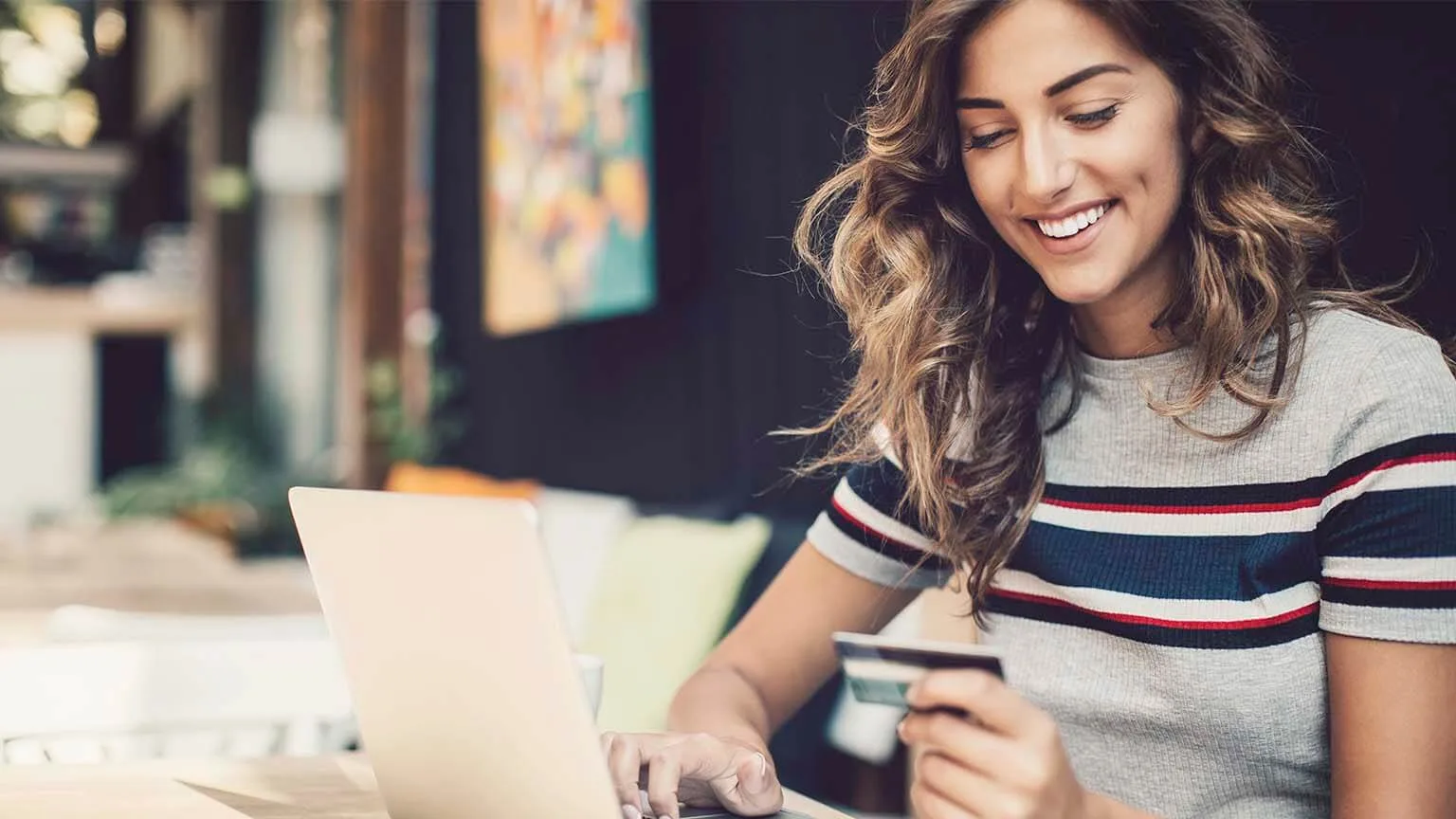 Image: Getty Images Smiling young woman holding a debit card and typing on a laptop