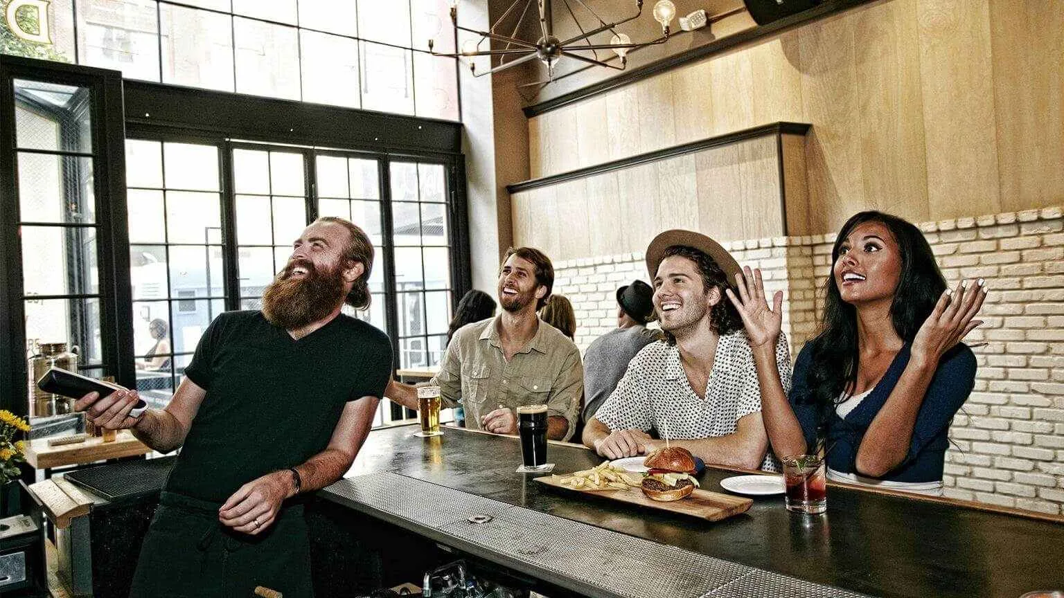 Image: Getty Images Smiling bartender and customers watching television in bar