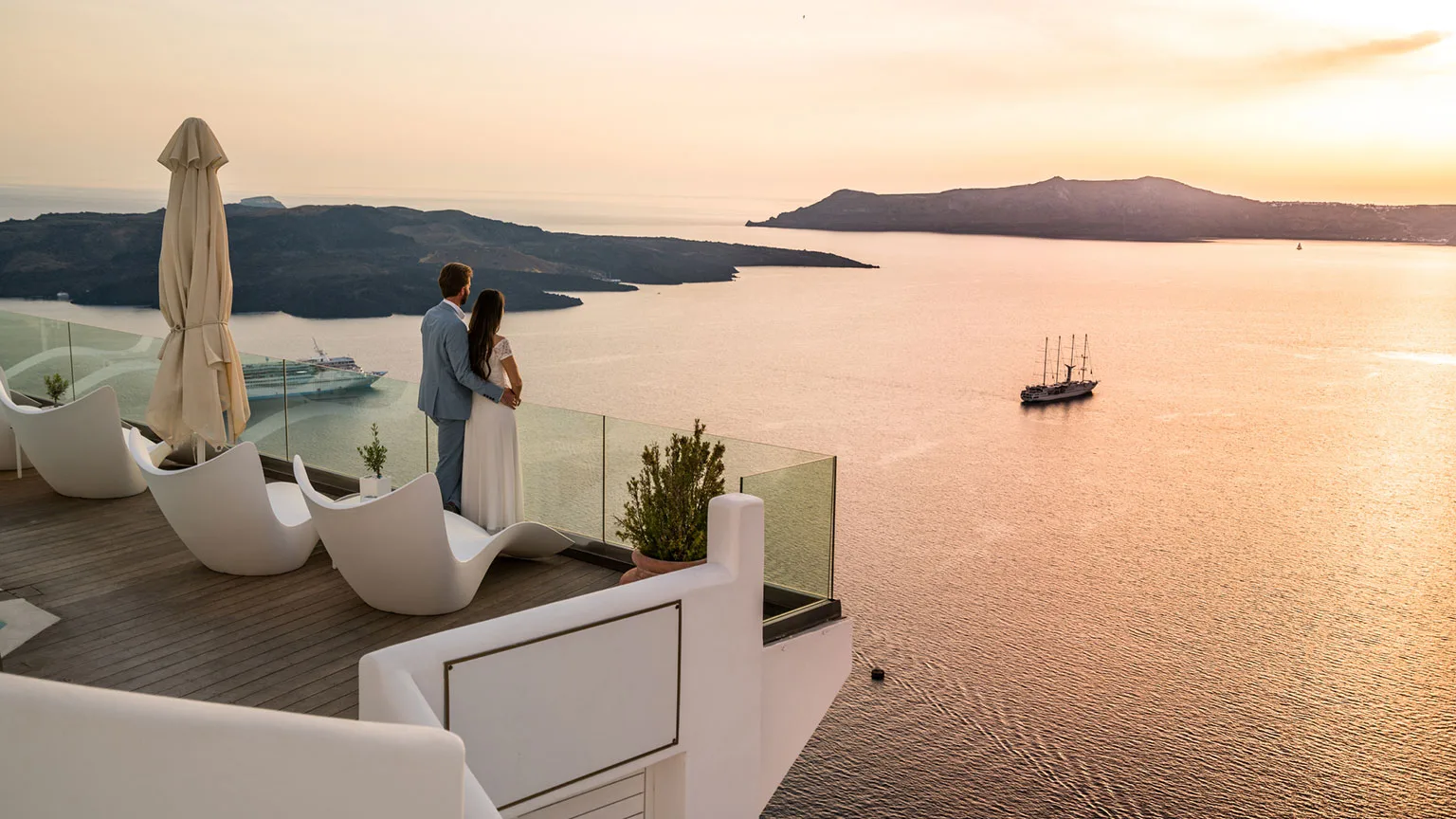Image: Getty Images Couple on balcony overlooking water in Greece at sunset