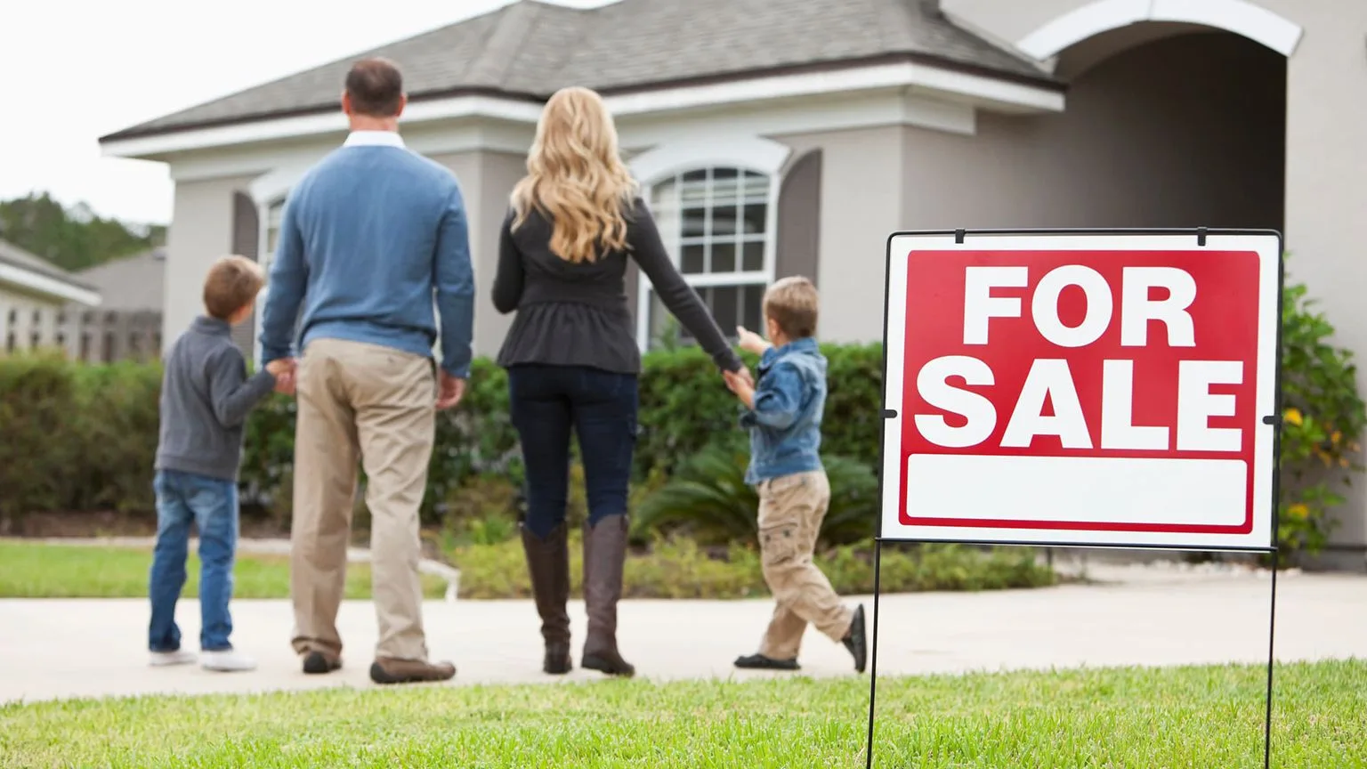 Image: Getty Images Family with two boys standing in front of house with for sale sign in front yard