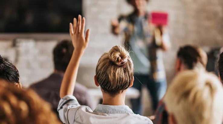Image: Getty Images Rear view of casual businesswoman raising her hand to ask the question on education event in a board room.