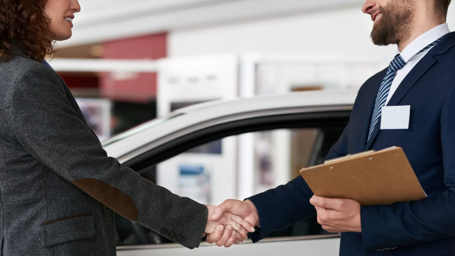 Image: Getty Images Two people shaking hands at an auto dealership