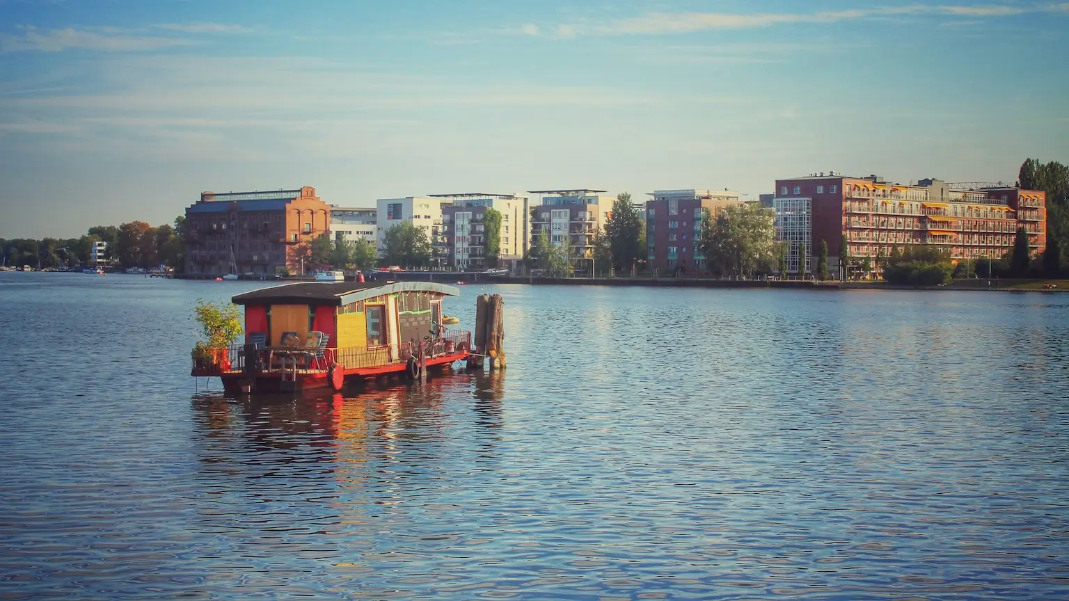 Image: Getty Images Houseboat moored in the middle of a river with view of the city on the shore.