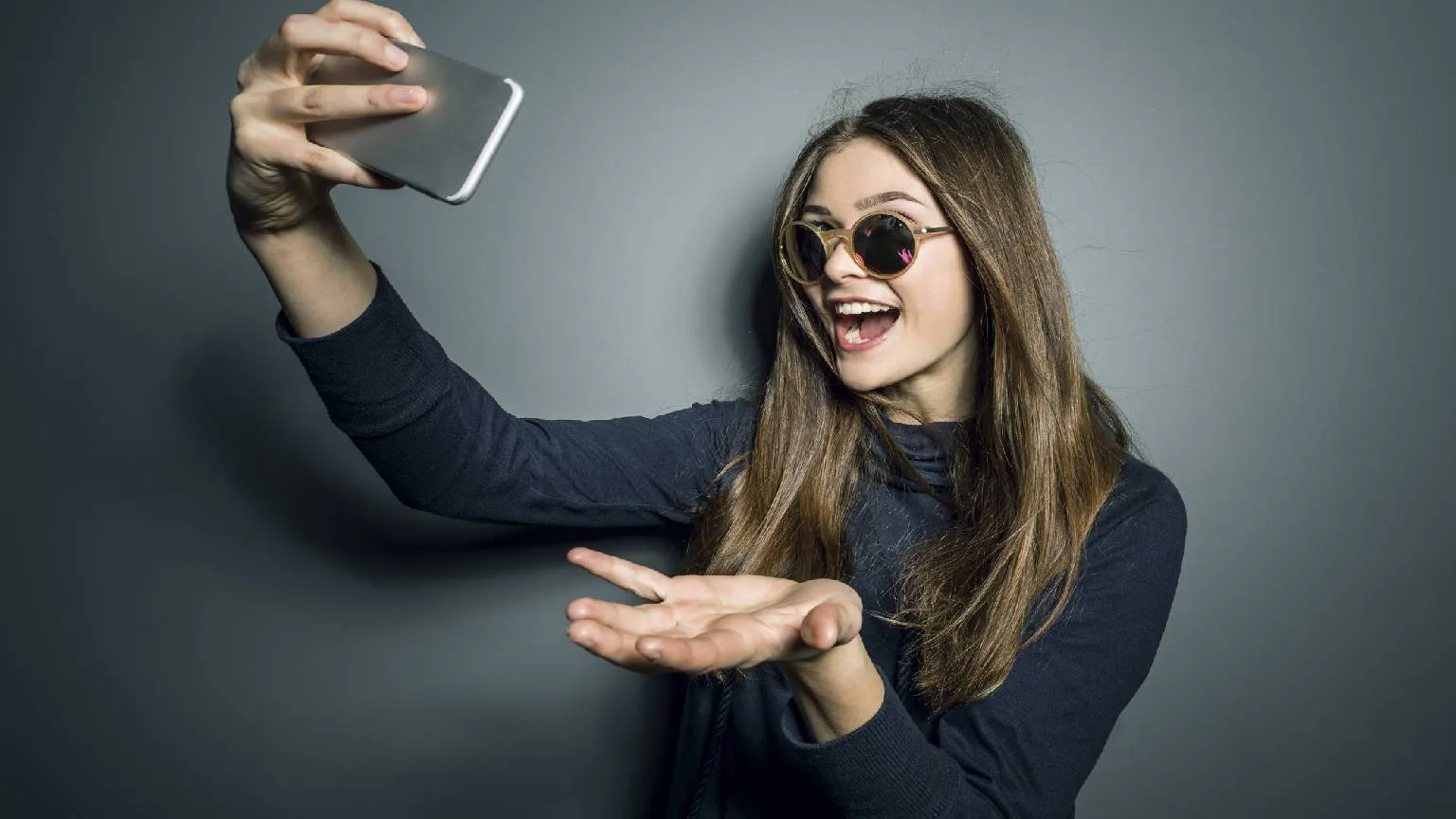 Image: Getty Images Girl with sunglasses smiling and taking selfie on cell phone.