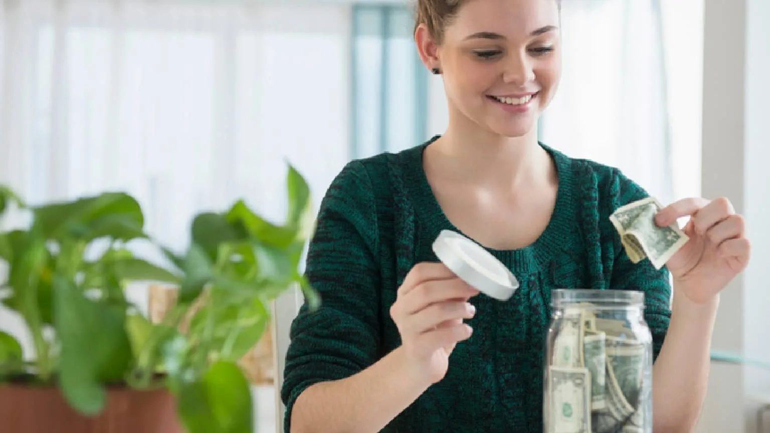 Image: Getty Images a teenager putting cash money in a glass far and smiling