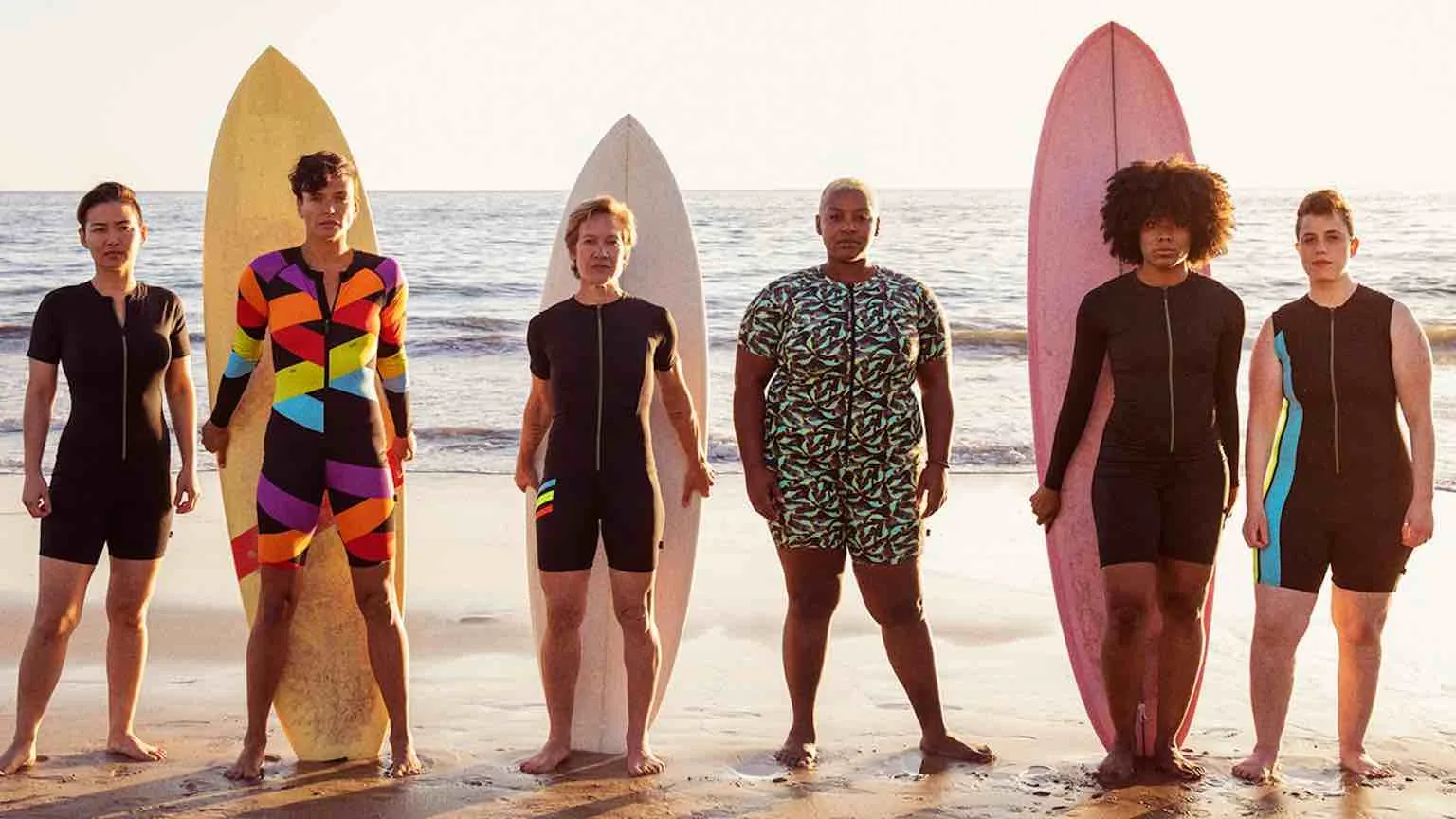 Tomboyx Group of surfers wearing Tomboyx clothing and posing near the ocean