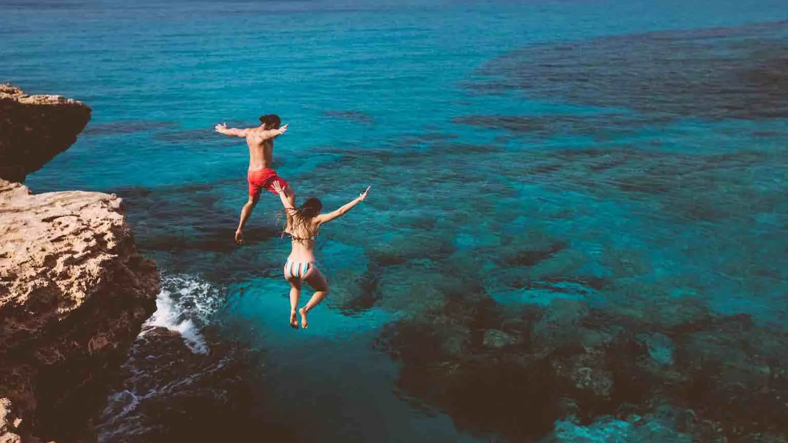 Young brave divers couple jumping off cliff into ocean Young brave divers couple jumping off cliff into ocean