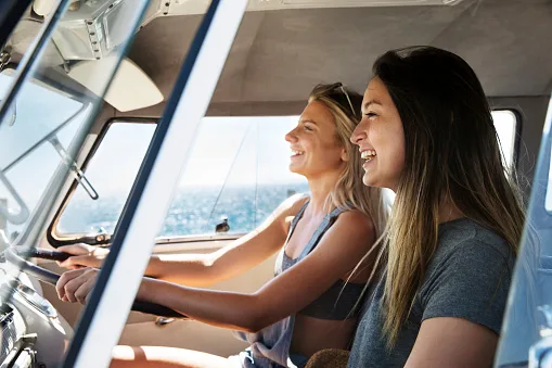 Image: Getty Images Two young women driving in a car on a road trip