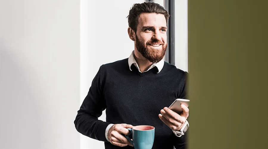 Image: Getty Images Happy employee standing in office with smartphone