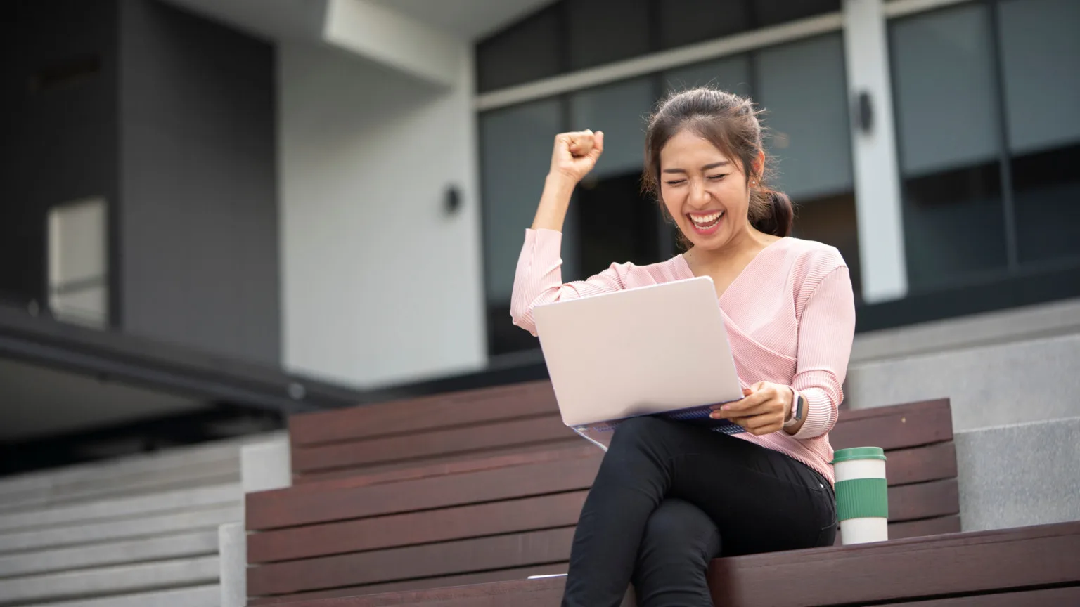 Image: Getty Images Woman sitting with her laptop outdoors on steps, cheering