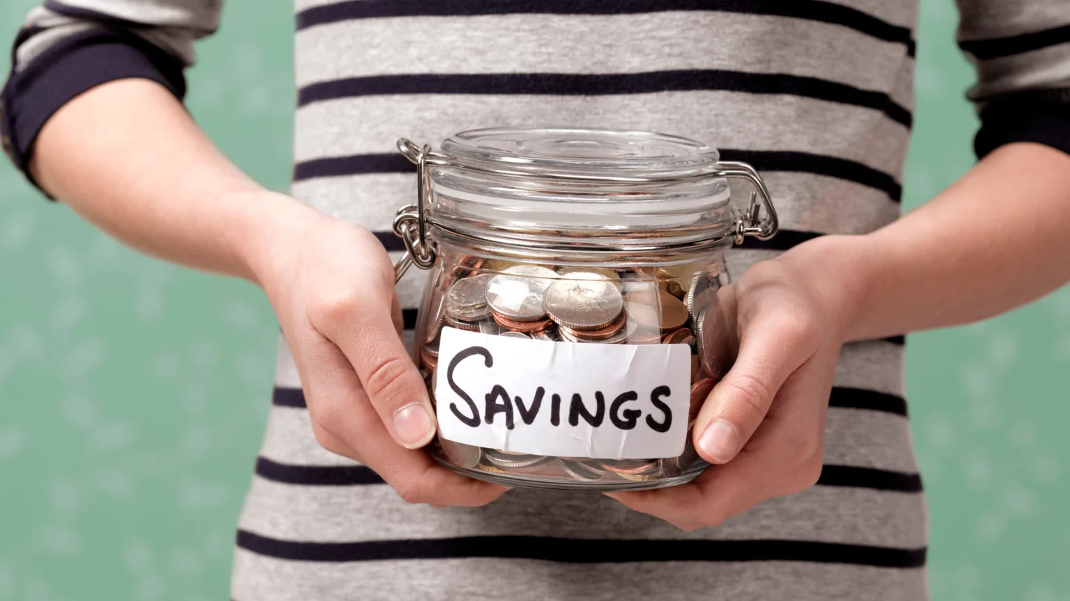 Image: Getty Images Close up of hands holding savings jar of coins