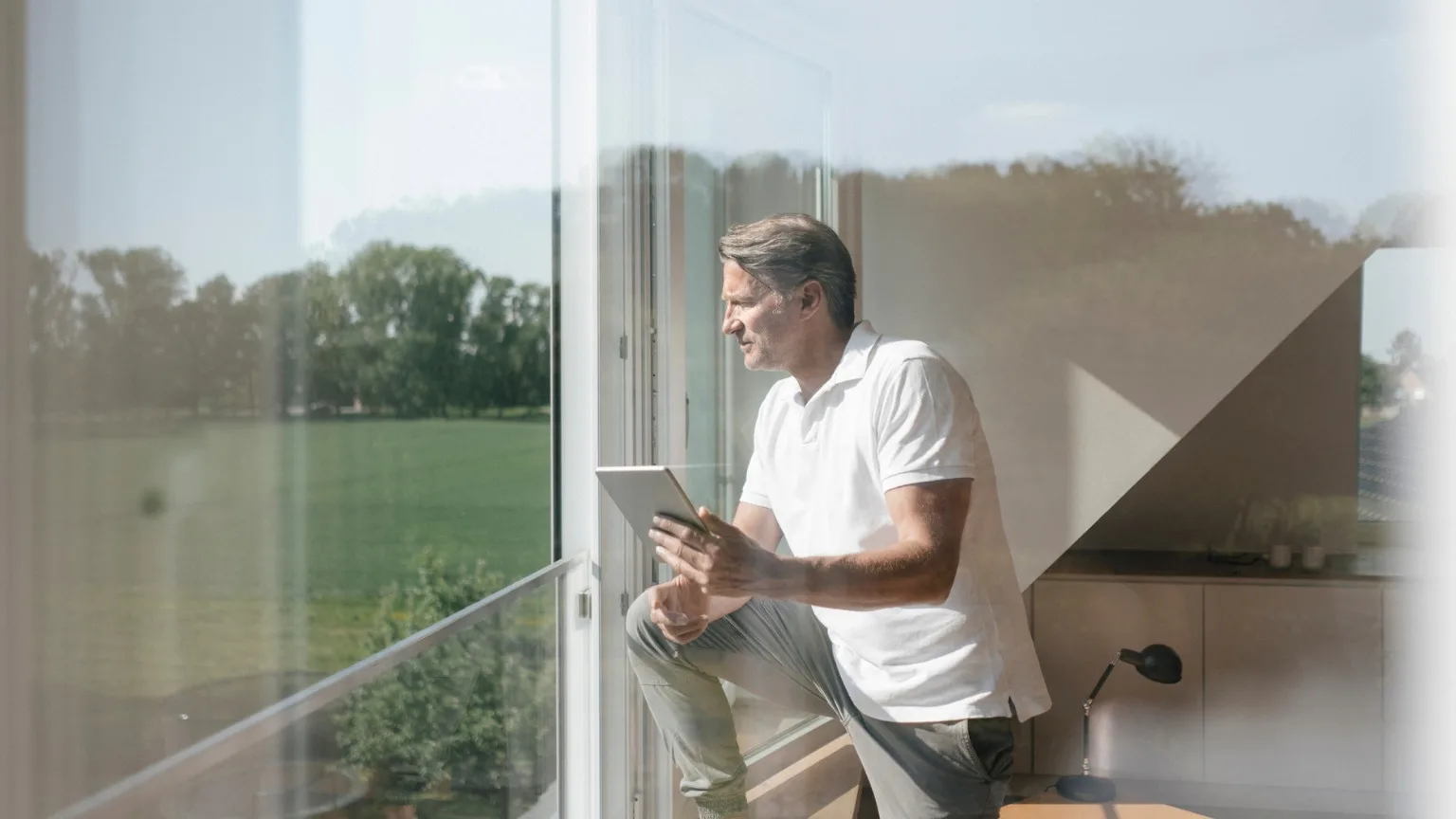 Image: Getty Images Man looking outside window thinking about how his investment in a cashable GIC will benefit his family's future and protect his principal.