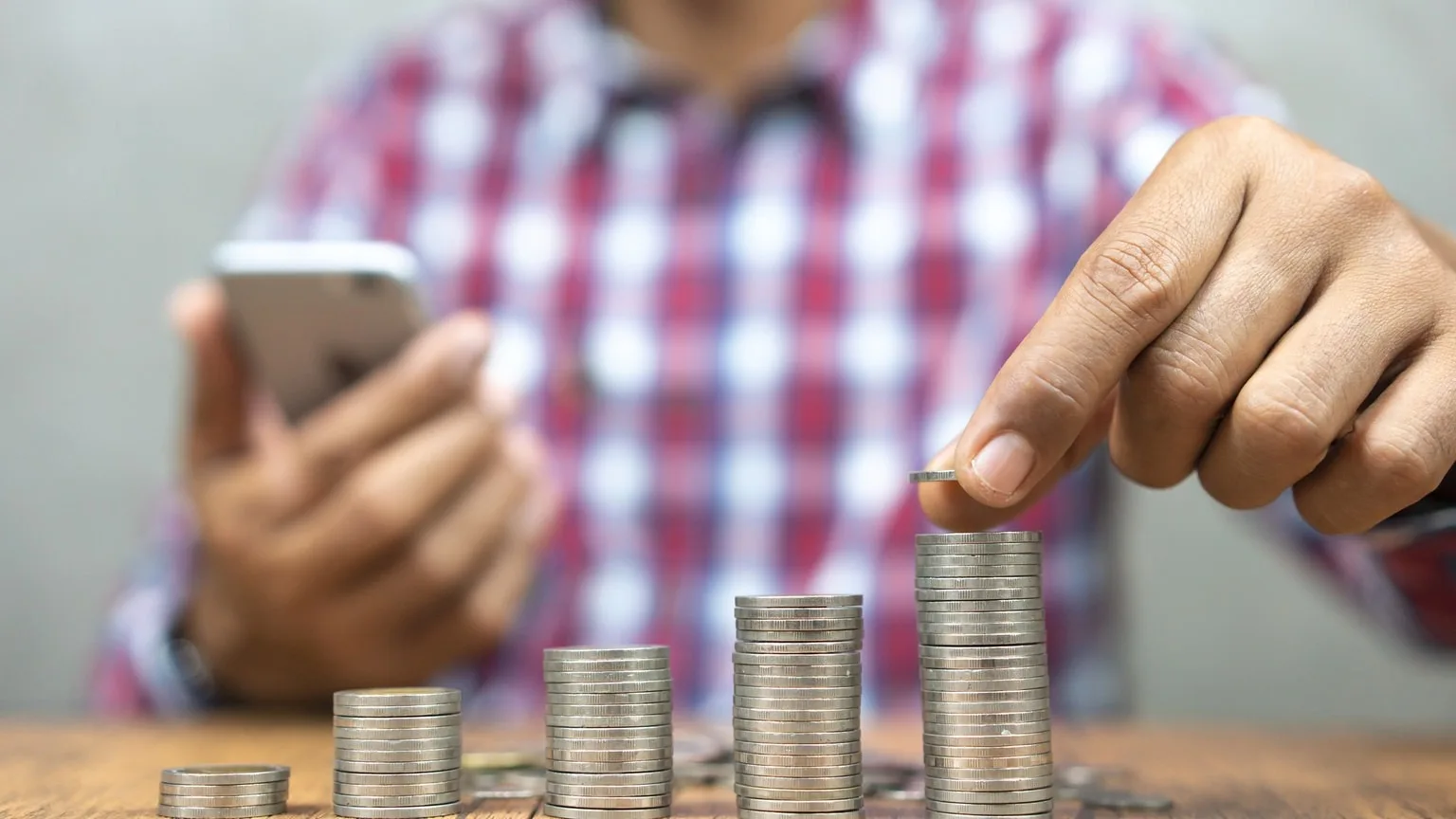 Image: Getty Images Male stacking coins while calculating on smart phone