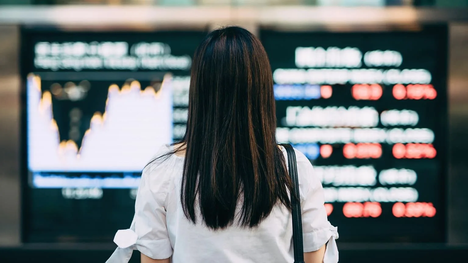 Image: Getty Images Rear view of businesswoman looking at stock exchange market display screen