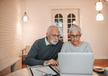 Senior couple checking savings accounts in a laptop in a domestic interio