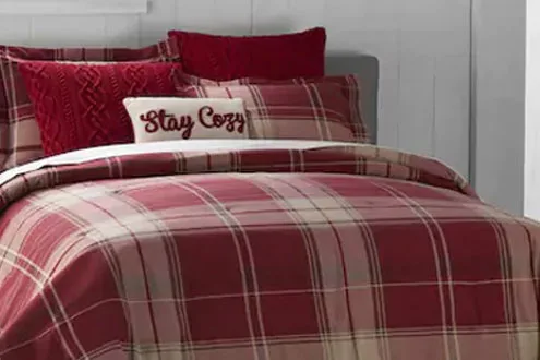Bed with red bedding and a pillow written stay cozy